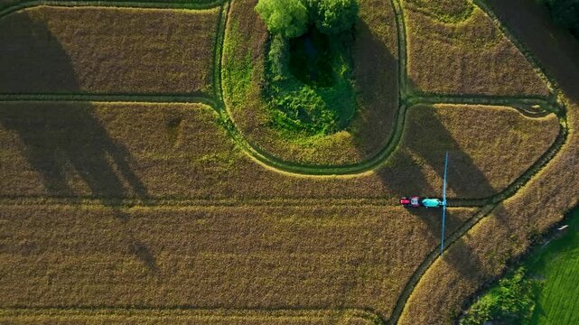 Tractor with Boom Sprayer Circles Round Pond in Field, Aerial Top Down