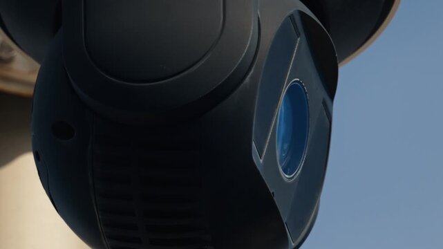 Close up of modern dark surveillance camera moving against blue sky.