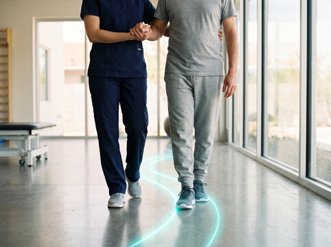 A physical therapist helps a male patient walk along a digital trajectory line during rehabilitation therapy.