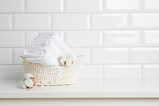 Basket with folded fresh towels on table in bathroom with copy space over white ceramic tile background
