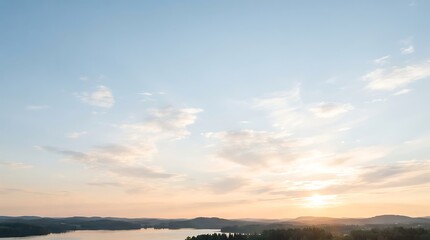 Obraz premium Panoramic view of a serene lake surrounded by dark forests under a vast sky with soft clouds during sunrise or sunset.