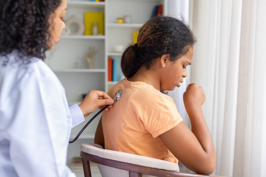 Black female doctor listening to coughing young girls back with stethoscope during checkup, illustrating respiratory examination and pediatric medical care