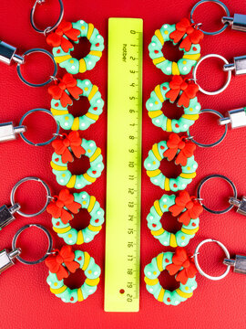 Christmas wreath keychain designs in a close-up view, featuring green evergreen loops, small festive accents, and a glossy finish. Sparkling highlights on a red background.