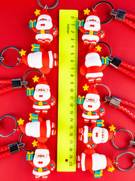 A set of 10 identical Santa keychain figures. Close-up view highlights the glossy red suit, white trim, and a friendly smiling face, festive sparkle on a red background.