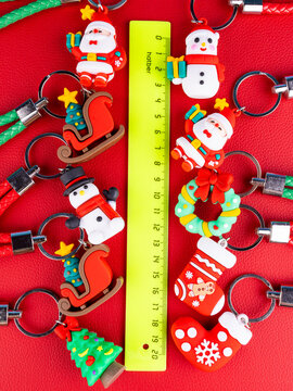 A bundle of seasonal key rings: Santa, a reindeer, a Christmas evergreen, a snowman and more. Crisp close-up textures, glossy accents, sparkling highlights on a red background.