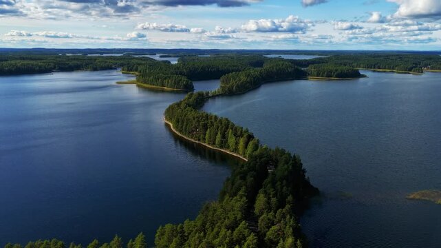 Aerial view of the narrow Punkaharju ridge winding through deep blue lakes and lush pine forests under a bright sky in Savonlinna, South Savo, Finland.