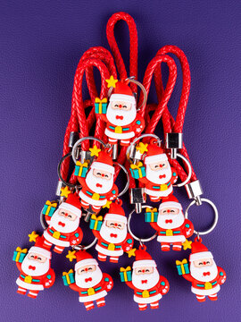 A set of 10 identical Santa keychain figures. Close-up view highlights the glossy red suit, white trim, and a friendly smiling face, festive sparkle on a purple background.