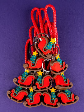 A set of 10 identical sleigh keychains, each featuring a small Christmas tree. Close-up view shows glossy red and green details, bright reflections, and a festive sparkle on a purple background.