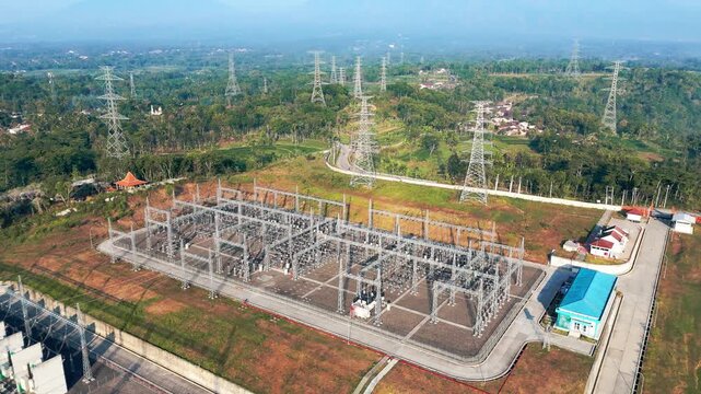 Aerial view of Ampel 150kV Substation with Mount Merbabu and Mount Merapi in the background, surrounded by hills and power towers in Kecamatan Ampel, Jawa Tengah, Indonesia.