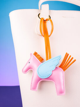 Close-up of a pink leather Pegasus bag charm with wings attached to a white handbag. Elegant fashion accessory with delicate details, perfect for handbags, everyday outfits, gifts and stylish looks.