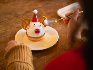 Woman eating cute Christmas reindeer cupcake with spoon on wooden table © Oil And Den