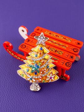 Close-up of a gold Christmas brooch in the shape of a Christmas tree, adorned with festive decorations and ornaments
