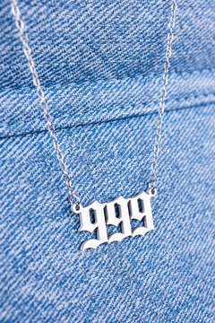 Close-up of a silver   pendant with the number 999 on a chain, set against a  blue background.