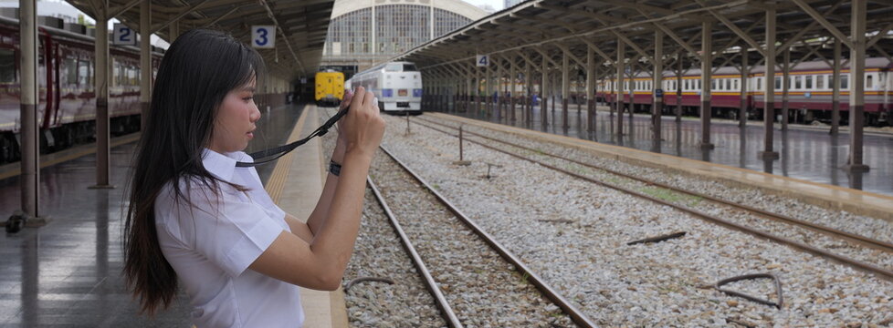 A young Asian woman with long black hair in a white short-sleeved university uniform takes photos with a small camera