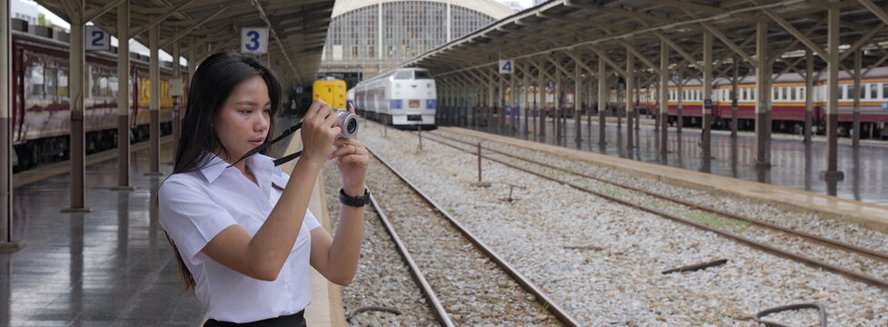 A young Asian woman with long black hair in a white short-sleeved university uniform takes photos with a small camera
