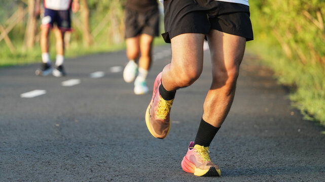 Close-up view of runners wearing colorful running shoes while training together on a scenic outdoor road in warm sunlight