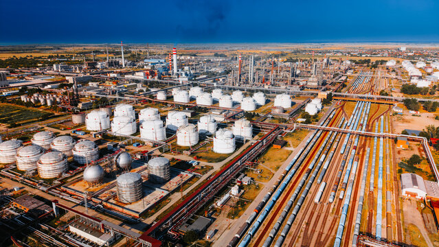 Aerial shot of oil refinery storage tanks and train cargo tracks.. High angle view of white liquid reservoirs, spherical containers, blue train cars, clear blue sky.