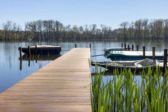 Wooden pier stretching across calm water with covered boats docked near lush green lake plants in Nieuwdonk Belgium
