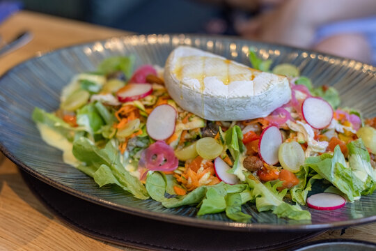 Fresh cheese salad with sliced radishes, grapes, and honey drizzle served on a decorative plate