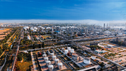 Fototapeta premium Industrial area with tanks and pipelines under blue sky in daytime. Aerial view of an industrial zone showing storage tanks and pipelines in the city.