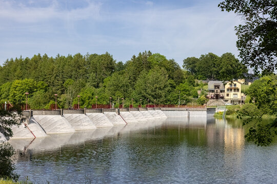 Concrete dam wall surrounded by lush green forest landscape and calm waters at Lake B&uuml;tgenbach in Belgium