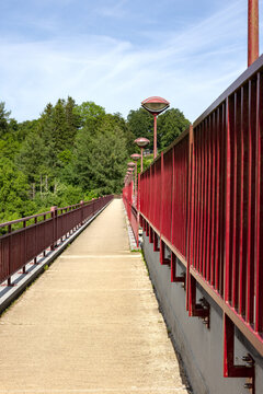 Long pedestrian walkway on top of a dam lined with red metal railings and street lamps at Lake B&uuml;tgenbach in Belgium