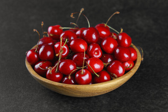 Fresh ripe sweet cherries in rustic wooden bowl on black stone textured background with copy space for text. Juicy organic summer fruit, red berries, healthy seasonal food, farm harvest