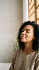 Fototapeta premium African American woman with closed eyes enjoying peaceful sunlight at home. Mindfulness, relaxation, self-care, emotional wellness, and tranquil lifestyle concept with copy space.