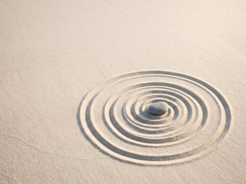 Smooth stone surrounded by concentric circles drawn in sand. Zen meditation concept representing mindfulness, balance, calm, focus, harmony, and inner peace with copy space.
