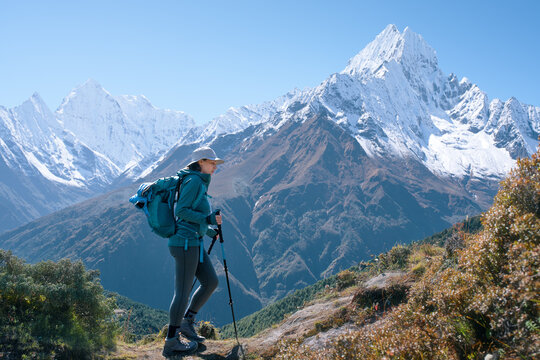 Female hiker with backpack and trekking poles walking on mountain trail with majestic Mount Ama Dablam in background, Nepal Himalayas.
