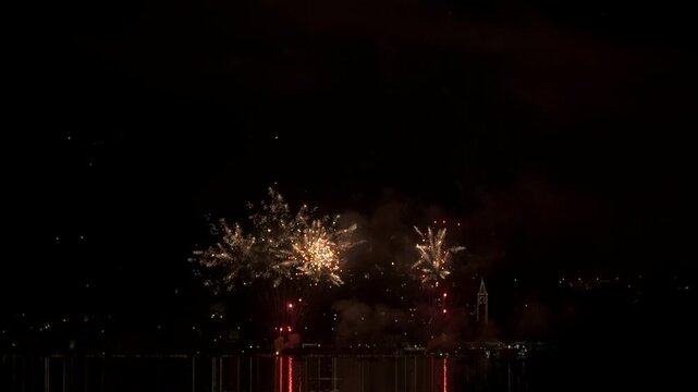 A fireworks display in the small town of Pusiano, in northern Italy. The multicolored fireworks sparkle in the sky and reflect in the water of the lake. In slow motion
