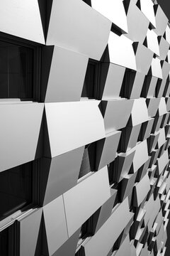 Across a monochrome facade, angular panels project through the frame, while windows recede into shadows and geometric repetition builds depth and a strong visual rhythm
