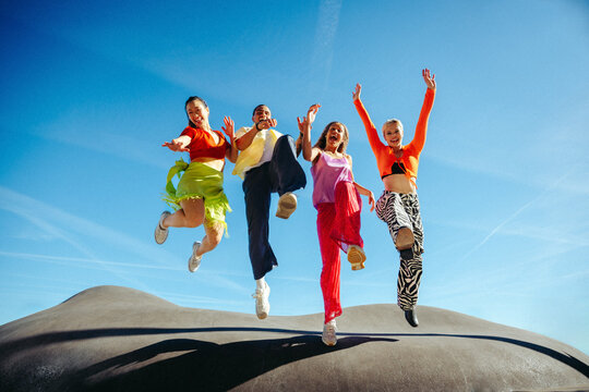 Friends leap joyfully together in outdoor celebration under blue sky