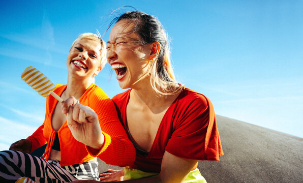Young women enjoy popsicles and laughter under the summer sky