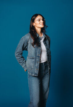 Her denim look frames a woman standing on a blue studio background
