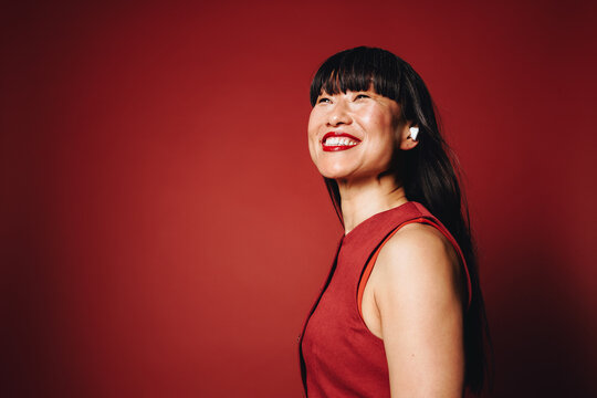 Woman wearing earbuds and smiling in red studio portrait