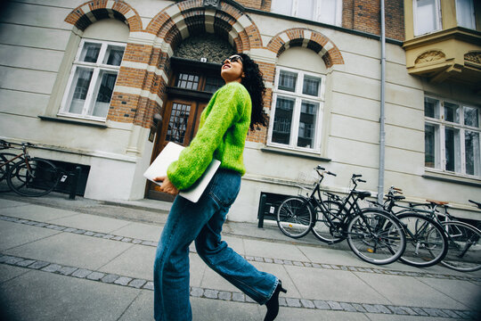 The woman walks with a laptop through the city for work on the go