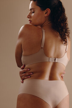 Woman in nude underwear embracing her own curvy body