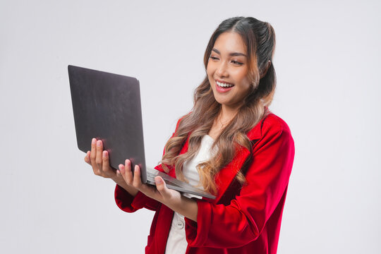 Smiling young Asian woman wearing red jacket holding laptop to work or browsing.