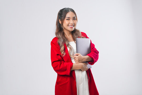 Joyful young Asian woman wearing red jacket holding laptop while smiling.