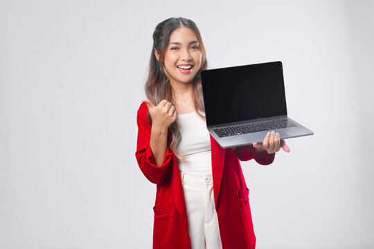 Smiling young Asian woman presenting copy space on her laptop while showing thumb up gesture.