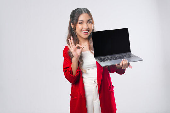 Pretty young Asian woman presenting copy space on her laptop while showing okay finger gesture.