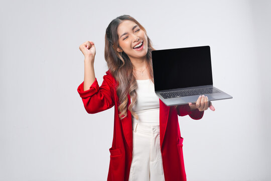 Excited young Asian woman raising her fists doing celebration while presenting laptop.