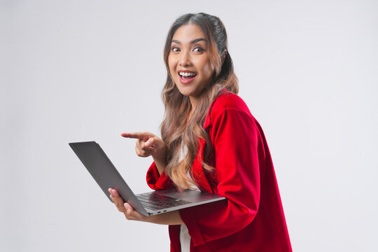Attractive young Asian woman in red jacket pointing to the laptop computer she holds.