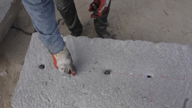 Japanese stonemason kneels to drive wedges into a row of drilled holes along a chalk line, splitting a large granite slab by hand