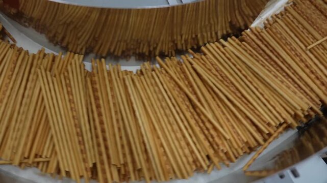Huge quantity of thin baked sticks gathering in a curved accumulator bowl on a snack production line