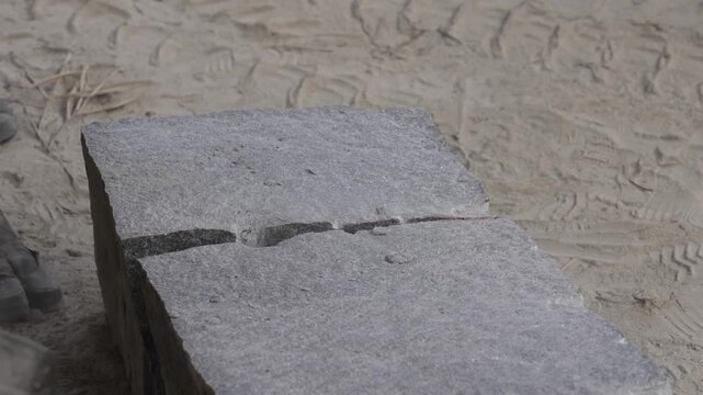 Close up of a granite block splitting cleanly in two as a stonemason drives a steel wedge along the drilled line