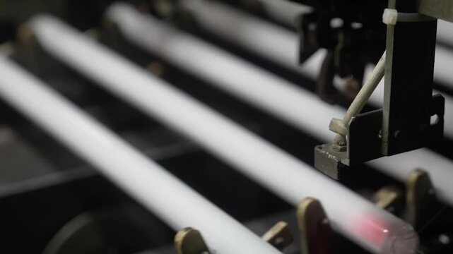 Finished fluorescent tubes moving along a conveyor past red laser markers in a Japanese lighting plant