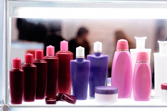 Colorful cosmetic bottles and skincare jars arranged on a backlit shelf, showcasing pink, purple and red packaging for shampoo, lotion and creams in a retail, salon or spa setting.