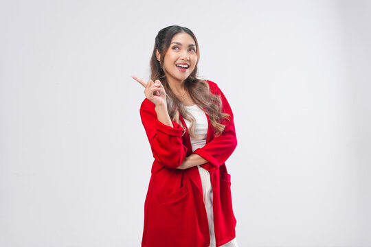 Smiling young Asian woman wearing red jacket is pointing to the copy space behind her.